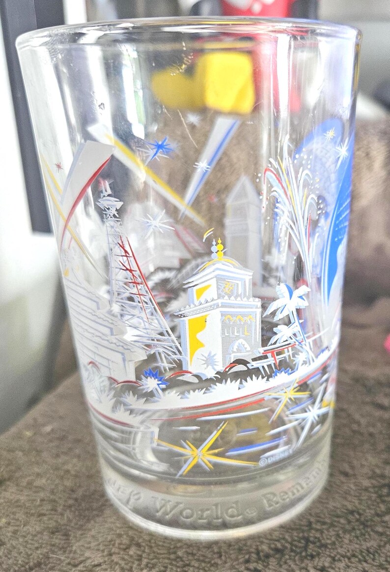 May include: Clear glass with a colorful illustration of a cityscape, fireworks, and the text "World Remember". The design includes white, yellow, red, and blue accents. The glass has a slightly flared shape.