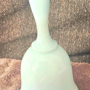 Könnte beinhalten: Ein hellgrünes, glockenförmiges Dekorationsstück mit einem langen, schlanken Griff. Die Glocke hat einen abgerundeten Boden und eine glatte, glänzende Oberfläche. Der Artikel ist wahrscheinlich aus Glas oder Keramik.