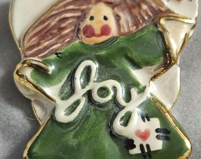 Vintage clay angel featuring a child-like drawing in a green dress, with joy depicted on her chest.