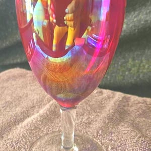 Peut inclure: Un verre à vin rouge avec une tige et une base transparentes. Le verre reflète un arc-en-ciel de couleurs, créant un effet chatoyant. Le verre est posé sur une surface texturée.
