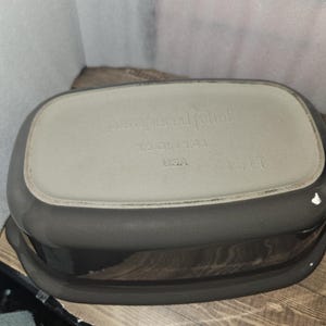 May include: A dark gray rectangular Pampered Chef baking dish. The bottom of the dish is light gray with the words "pampered chef", "1.5 QT/1.4 L", and "USA" printed on it. The dish has a capacity of 1.5 quarts or 1.4 liters.