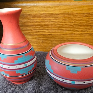 May include: A set of two red ceramic vases with a Southwestern design. The vases are decorated with geometric patterns in turquoise, white, and gold.