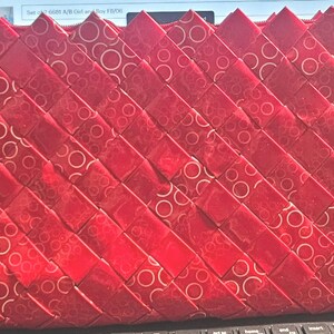 K&ouml;nnte beinhalten: Eine rote gewebte Clutch mit Rei&szlig;verschluss. Die Clutch besteht aus einem gl&auml;nzenden Material mit einem Muster aus wei&szlig;en Kreisen. Das Gewebe ist diagonal und erzeugt eine strukturierte Oberfl&auml;che. Der obere Rand hat ein Zickzack-Design.