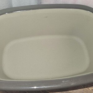 May include: A gray ceramic baking dish with a rectangular interior and rounded corners. The dish has a light gray interior and a darker gray rim and handles. This kitchenware is suitable for baking and serving.