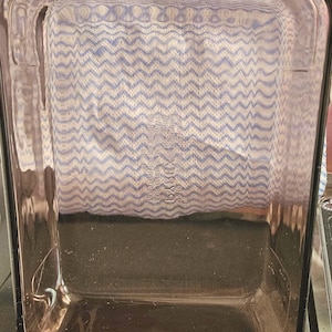 Könnte beinhalten: Eine rechteckige Pyrex-Backform aus klarem, braun getöntem Glas. Die Form hat ein schlichtes, funktionales Design mit geraden Seiten und einem flachen Boden. Das Pyrex-Logo ist sichtbar. Im Hintergrund ist ein blau-weiß gemustertes Tuch zu sehen.