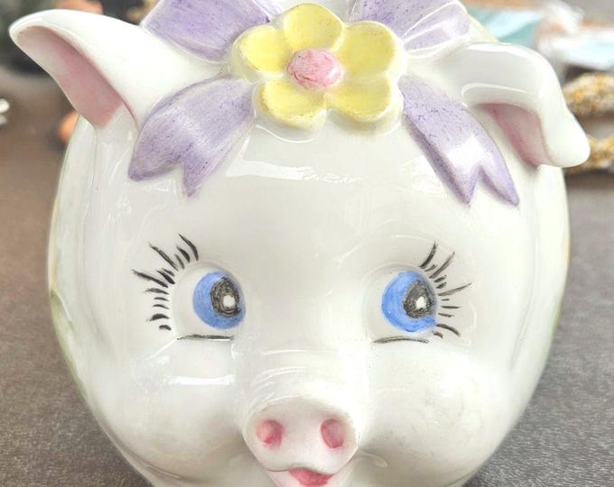 Vintage glass piggy bank inscribed with "Sept. 10, 1964," featuring white color with yellow flowers on its side and a purple ribbon, C7/13