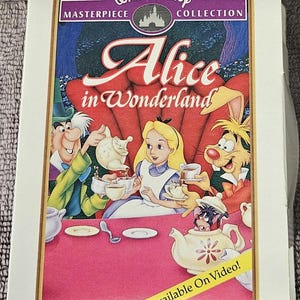 May include: A vintage VHS tape case featuring a colorful illustration of Alice in Wonderland characters, including Alice, the Mad Hatter, and the March Hare, having tea. The text on the case reads "Walt Disney Masterpiece Collection Alice in Wonderland Available On Video!"