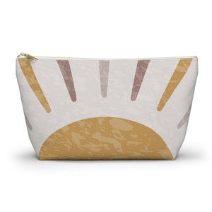 May include: A white canvas zippered pouch with a graphic of a yellow sun with pink rays.