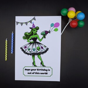 Puede incluir: Tarjeta de cumpleaños con una ilustración de un extraterrestre verde sosteniendo una pistola de rayos y globos. La tarjeta dice "Hope your birthday is out of this world!" con una pancarta y velas. Globos de colores adjuntos.