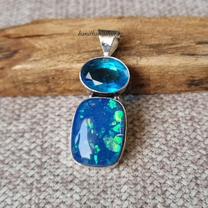 May include: A silver pendant featuring two gemstones. The top stone is an oval, faceted, light blue gem. The bottom stone is a rectangular, dark blue opal with green and blue flashes. The pendant has a silver bail and the text "banithanilsilver07".