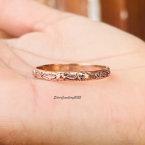 May include: A bronze-colored ring with an intricate floral pattern. The ring is thin and has a detailed design of flowers and leaves. The text "SilverJewellery2025" is visible.