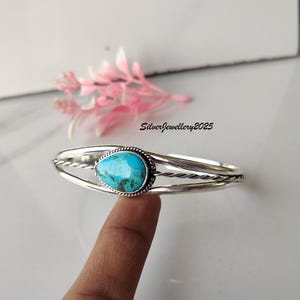 May include: A silver cuff bracelet featuring a turquoise teardrop-shaped stone. The stone is set in a beaded bezel. The bracelet has a twisted rope design. The text "SilverJewellery2025" is visible.