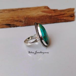 May include: A silver ring with a turquoise gemstone set in a bezel setting. The ring has a rope-like design around the edge of the bezel.
