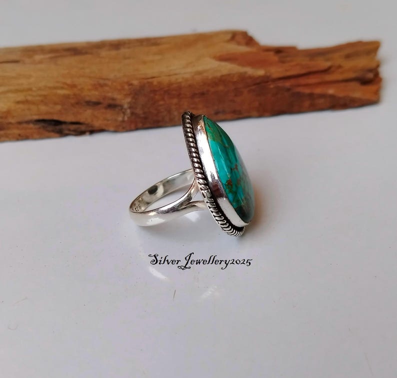May include: A silver ring with a turquoise gemstone set in a bezel setting. The ring has a rope-like design around the edge of the bezel.