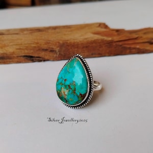 May include: A turquoise gemstone ring with a teardrop-shaped stone set in silver. The ring has a rope-like design around the stone.