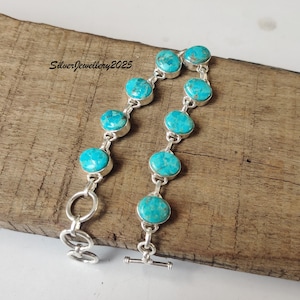 May include: A silver bracelet with turquoise gemstones. The bracelet has a toggle clasp and is shown on a wooden surface. The text "SilverJewellery2025" is visible in the upper left corner.