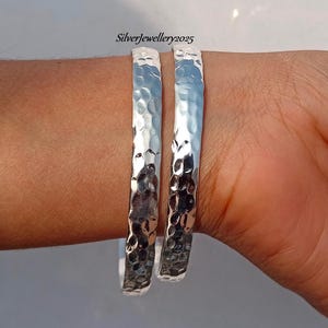 May include: Two silver hammered bangle bracelets. The bracelets are smooth and shiny, with a textured hammered finish.