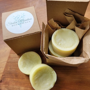 May include: Three round, pale green, handmade soap bars in a brown cardboard box with a white label that says "Shaker Mountain Botanicals".