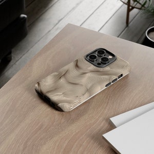 May include: A beige phone case with a black and white wavy pattern. The case has a raised camera bump with three lenses.