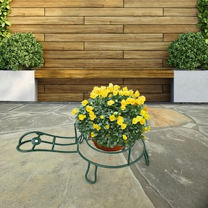 May include: A green metal turtle-shaped plant stand with a potted plant with yellow flowers. The stand is on a gray stone patio.
