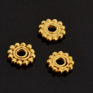 May include: Three gold-coloured metal bead spacers with a round hole in the centre. Each spacer is surrounded by a ring of small, raised dots.