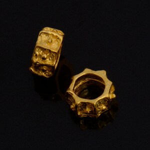 Peut inclure: Deux perles en m&eacute;tal de couleur dor&eacute;e avec une surface textur&eacute;e. Les perles sont rondes et ont un trou au centre.