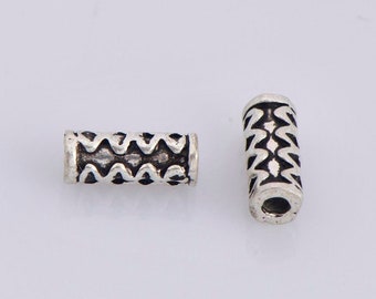 May include: Two silver metal spacer beads with a geometric design. The beads are cylindrical and have a hole in the center.