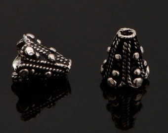 May include: Two silver cone-shaped bead caps with a decorative design of small circles and lines.