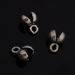 Könnte beinhalten: Drei silberfarbene Metallperlenkappen mit abgerundetem, offenem Design. Die Kappen haben eine kleine Schlaufe oben zum Anbringen an Schmuck oder andere Bastelarbeiten.