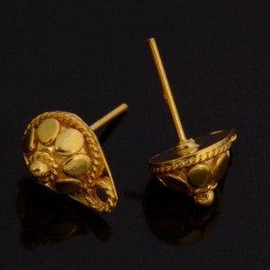 May include: A pair of gold earrings with a teardrop shape and a textured design. The earrings have a post back closure.
