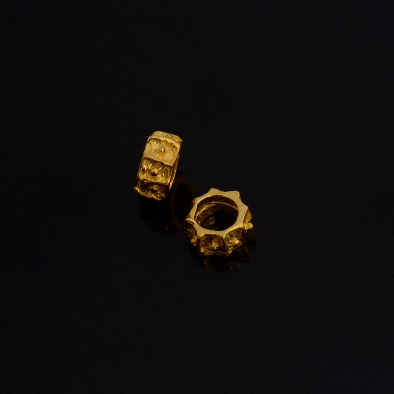 Peut inclure: Deux perles en m&eacute;tal de couleur dor&eacute;e avec une surface textur&eacute;e. Les perles sont rondes et ont un trou au centre.