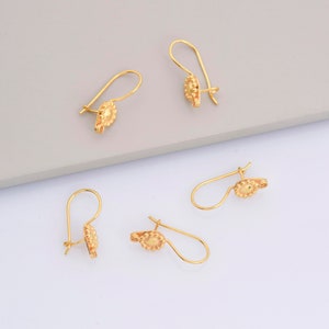 May include: Four gold-toned earring hooks with a textured circular design. The hooks are arranged in a staggered pattern on a white and gray surface.