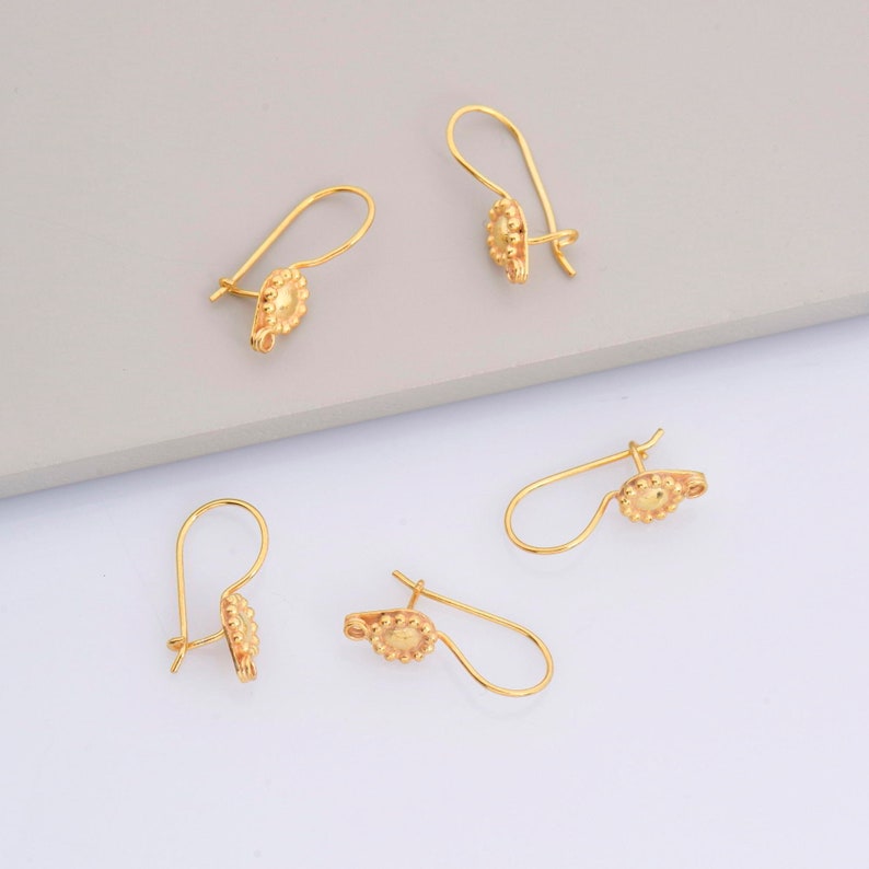 May include: Four gold-toned earring hooks with a textured circular design. The hooks are arranged in a staggered pattern on a white and gray surface.