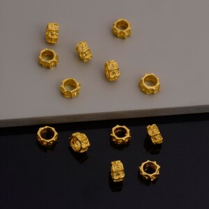 Peut inclure: Un ensemble de 14 perles en m&eacute;tal de couleur dor&eacute;e avec une surface textur&eacute;e. Les perles sont dispos&eacute;es de mani&egrave;re dispers&eacute;e sur une surface gris clair et une surface noire.