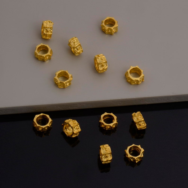 Peut inclure: Un ensemble de 14 perles en m&eacute;tal de couleur dor&eacute;e avec une surface textur&eacute;e. Les perles sont dispos&eacute;es de mani&egrave;re dispers&eacute;e sur une surface gris clair et une surface noire.