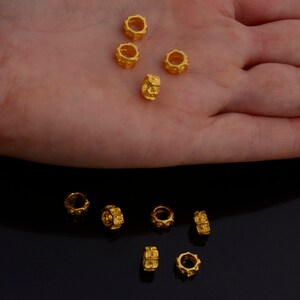 Peut inclure: Gros plan sur dix perles en m&eacute;tal de couleur dor&eacute;e avec une surface textur&eacute;e. Les perles sont dispos&eacute;es en deux rang&eacute;es sur une surface noire.