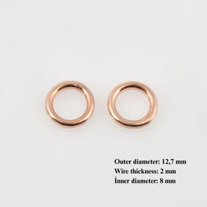 Peut inclure: Deux anneaux métalliques de couleur cuivre. Le diamètre extérieur est de 12,7 mm, l'épaisseur du fil est de 2 mm et le diamètre intérieur est de 8 mm. Les anneaux sont circulaires avec une finition lisse et polie.