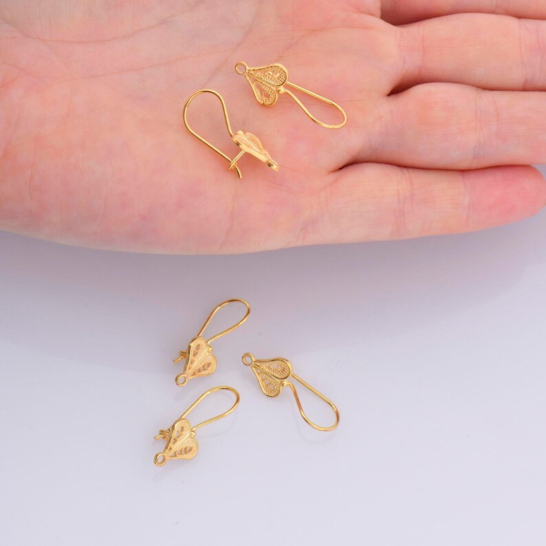 May include: Four gold-colored earring hooks with a delicate filigree design. The hooks are made of metal and have a loop at the top for attaching to earrings.