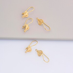 May include: Four gold-colored earring hooks with a delicate filigree design. The hooks are made of metal and have a loop at the top for attaching earrings.