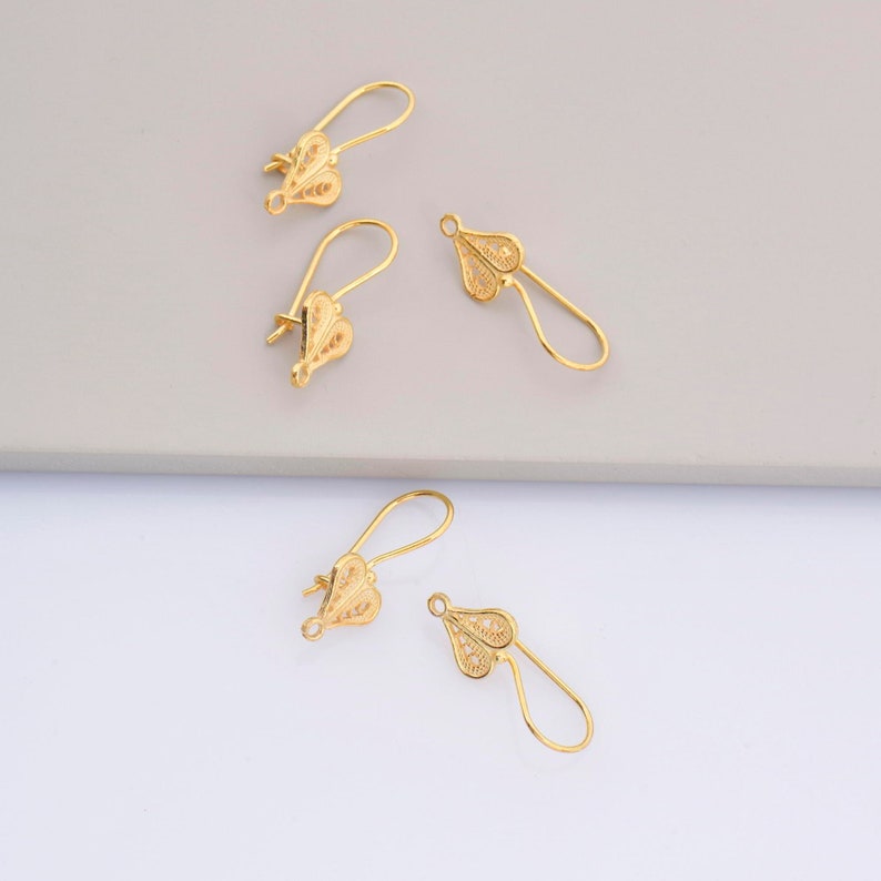 May include: Four gold-colored earring hooks with a delicate filigree design. The hooks are made of metal and have a loop at the top for attaching earrings.