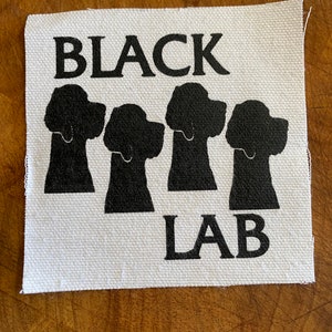 Puede incluir: Parche de tela blanco y negro con el texto "BLACK LAB" y cuatro siluetas negras de cabezas de Labrador Retriever.