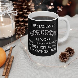 May include: A white ceramic mug with a black exterior, filled with a dark liquid. The mug features the text "I USE EXCESSIVE SARCASM AT WORK BECAUSE PUNCHING SOMEONE IN THE FUCKING FACE IS FROWNED UPON."