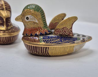 Può includere: Due scatole portagioie a forma di anatra con un intricato lavoro di smalto cloisonné. L'anatra in primo piano mostra vivaci motivi verdi, blu, rossi e dorati, mentre quella sullo sfondo presenta tonalità bordeaux e oro con finiture metalliche.