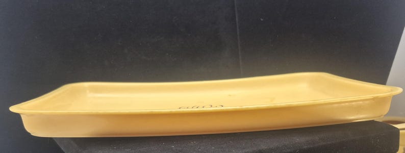 Pu&ograve; includere: Un vassoio rettangolare giallo chiaro con lati leggermente curvi. Il vassoio ha una superficie liscia e una profondit&agrave; ridotta. Gli angoli sono arrotondati e la forma generale &egrave; allungata. Il vassoio &egrave; appoggiato su una superficie nera.