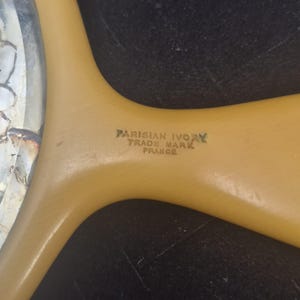 Pu&ograve; includere: Primo piano del manico di un pettine vintage Parisian Ivory. Il manico &egrave; di colore giallo chiaro con la scritta "PARISIAN IVORY TRADE MARK FRANCE" stampata in verde.