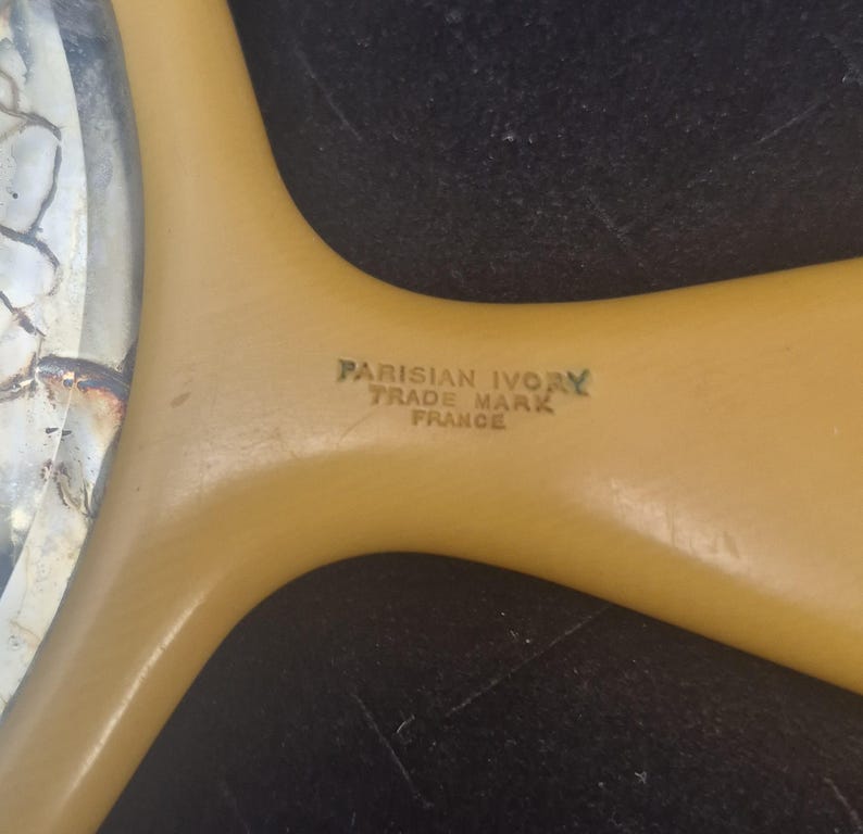 Pu&ograve; includere: Primo piano del manico di un pettine vintage Parisian Ivory. Il manico &egrave; di colore giallo chiaro con la scritta "PARISIAN IVORY TRADE MARK FRANCE" stampata in verde.