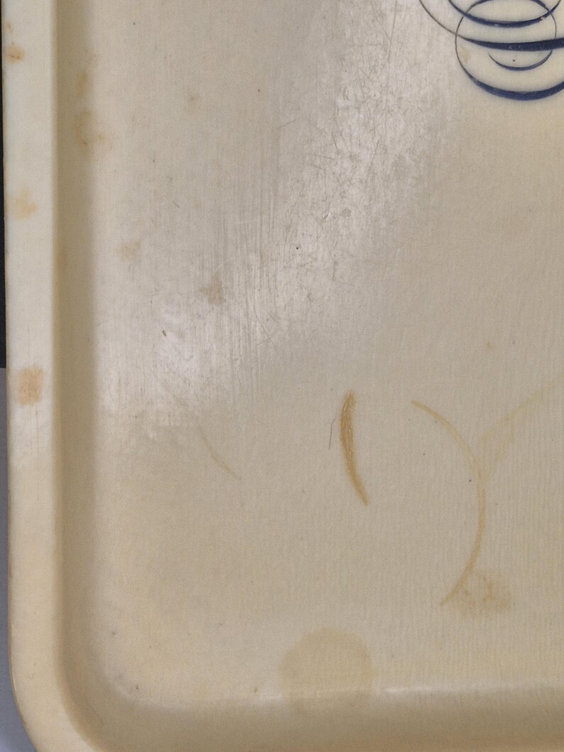 Pu&ograve; includere: Un vassoio rettangolare color crema con bordi arrotondati. Il vassoio presenta macchie e graffi visibili, che indicano un uso precedente. Un motivo a spirale decorativo blu e bianco &egrave; visibile nell'angolo in alto a destra. La superficie del vassoio mostra segni di usura.