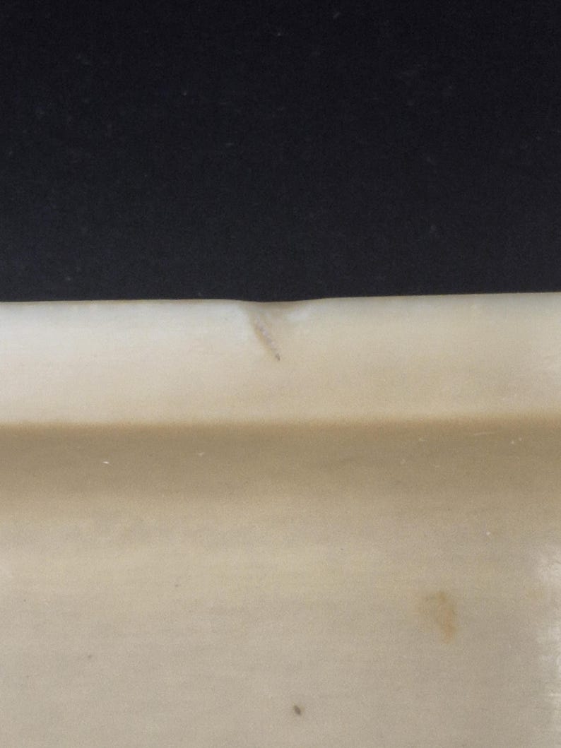 Pu&ograve; includere: Primo piano di un oggetto rettangolare beige chiaro su sfondo nero scuro. L'oggetto presenta una leggera rientranza e alcune piccole macchie. L'oggetto sembra essere fatto di un materiale solido.
