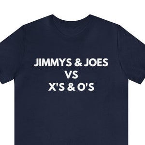 Puede incluir: Camiseta azul marino con el texto blanco "JIMMY'S & JOES VS X'S & O'S" en el pecho. La camiseta de manga corta está hecha de un material suave.