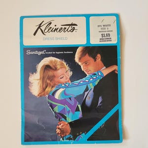 Puede incluir: Embalaje vintage de Kleiner's Dress Shield con borde azul. El paquete presenta una imagen retro de una pareja abrazándose. El texto en el paquete dice "Kleinert's Dress Shield" y "Sanitized treated for hygienic freshness".